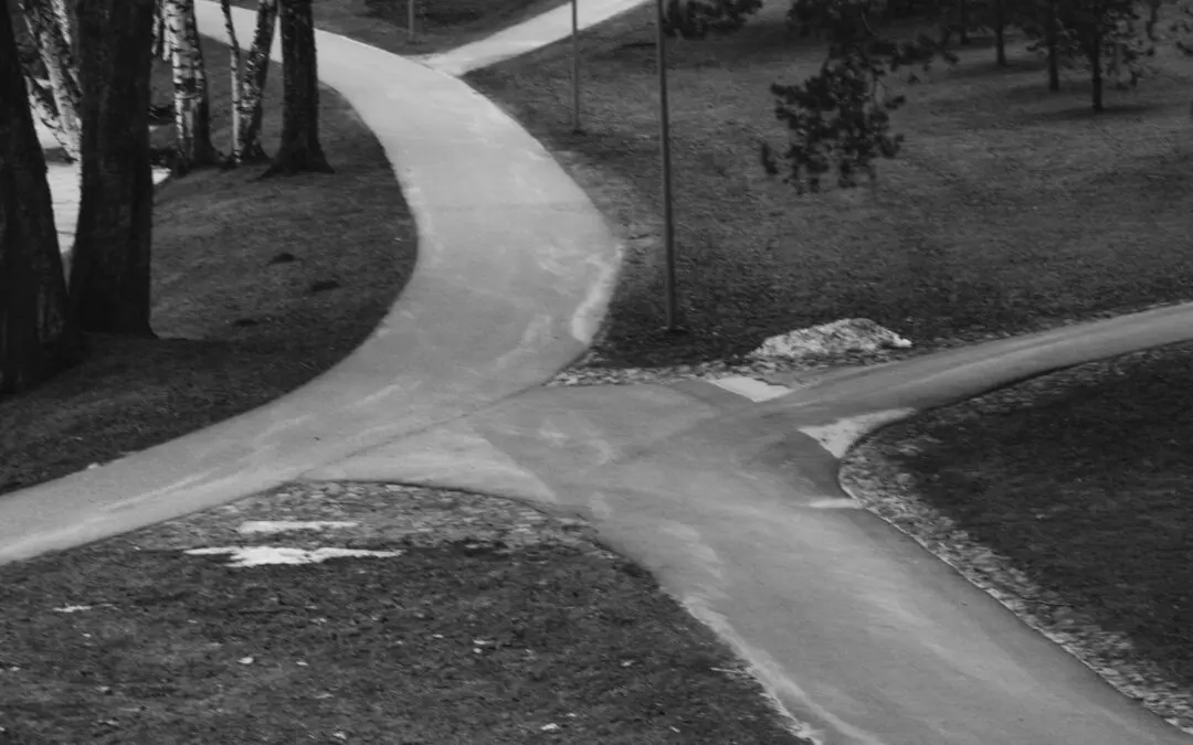 Black and white photograph of three paved park paths meeting at a junction, with worn ground beside them